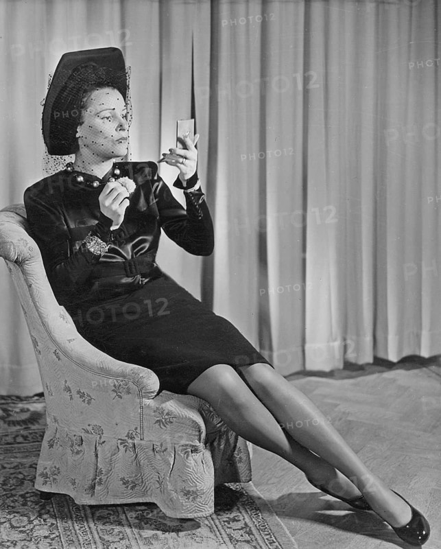 Swedish actress Margit Rosengren, 1901-1952. Pictured sitting in an armchair wearing a fashionable black dress, hat and veil. On her feet a pair of shiny black shoes and on her legs, nylon stockings. She looks herself in the mirror while bettering the makeup. Sweden 1945. Photo Kristoffersson