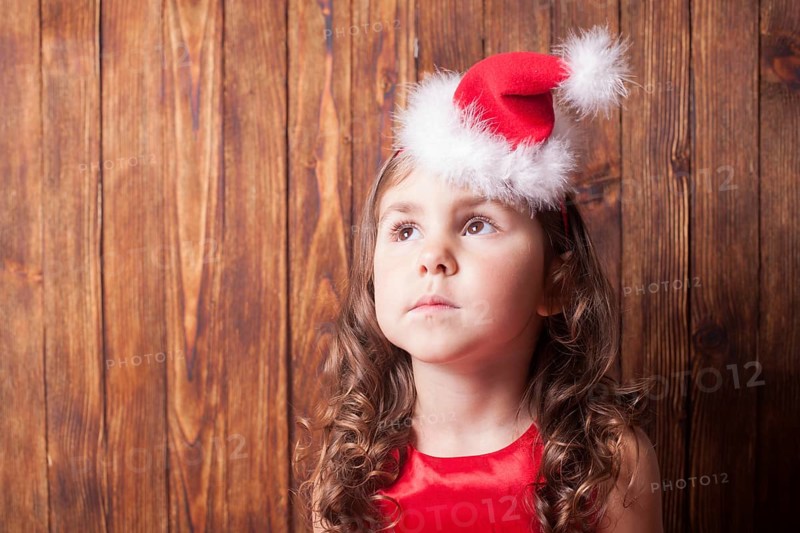 Girl in Santa hat headband sitting over wooden wall, copy space