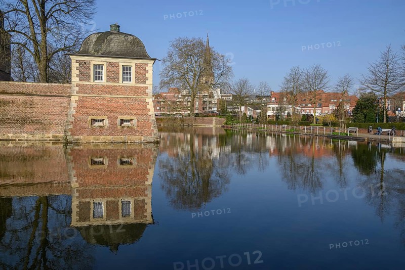 A pavilion at the moat with a clear reflection, surrounded by trees in the park in front of a blue sky, ahaus, münsterland, germany