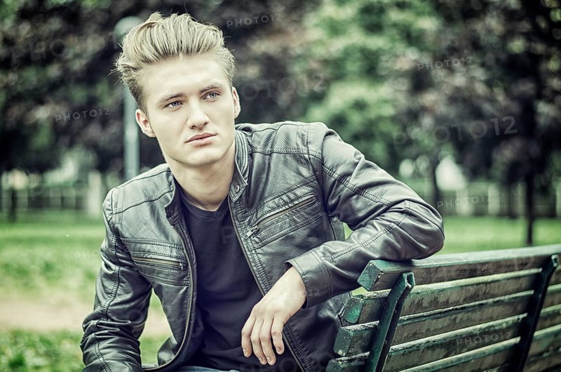 Handsome blond young man sitting on green, wooden park bench