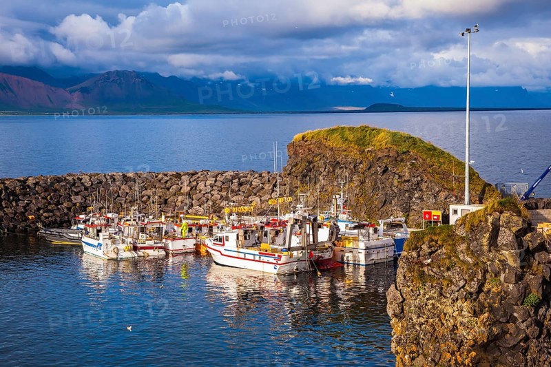 Sunset on the sea fjord in Iceland. White fishing boat in the harbor pier village Arnastapi