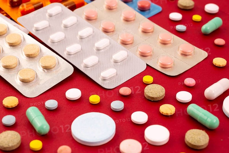 Different colorful pills and capsules in packs - blisters. Global pharmaceutical industry for billions dollars per year. Pharmaceutical drugs for use as medications. Isolated on a red background