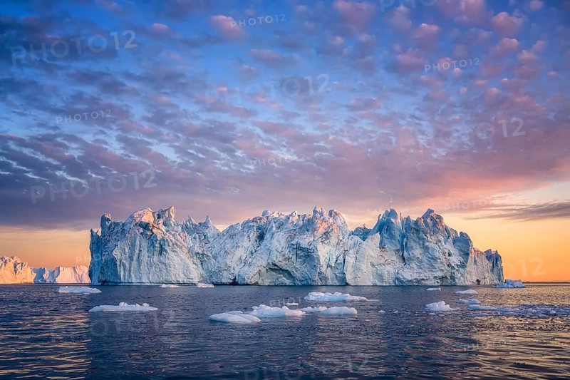 Large glaciers in the bay by the rocky shore in the light of the setting sun