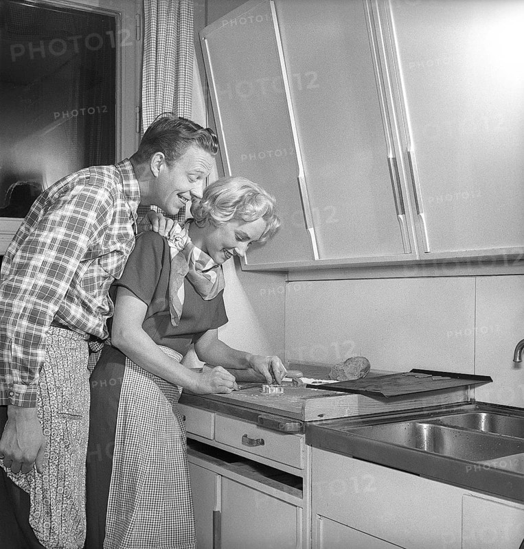 In the kitchen in the 1950s. Ayoung couple baking heart shaped gingerbread cookies for christmas. She puts the heartshaped metal form on the dough to make the shape. She is actress UllaCarin Rydén. Sweden 1951. ref Kristoffersson BE65-9