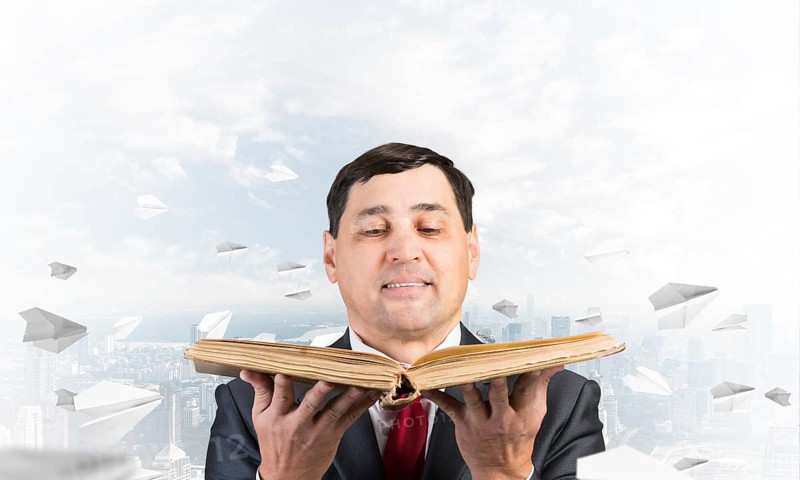 Happy businessman holding open old book. Smiling man in suit standing on downtown background with flying paper planes. Lawyer holding big legal regulation book. Business accounting and consulting