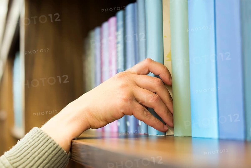 Hand pulling a book off the shelf. Blue colors books