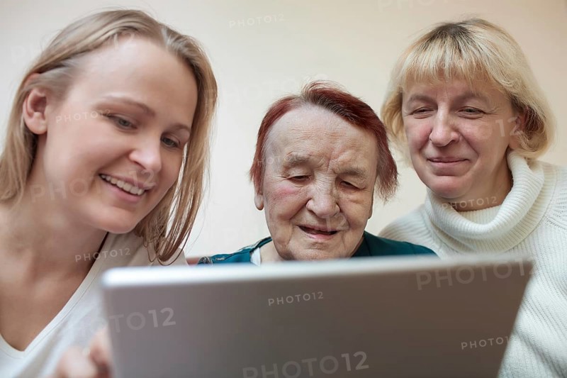 Three women of different ages smiling using a smart tablet