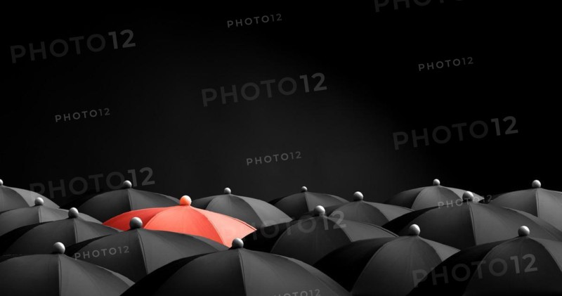 Concept image with lots of black umbrellas and a red umbrella that stands out, be unique