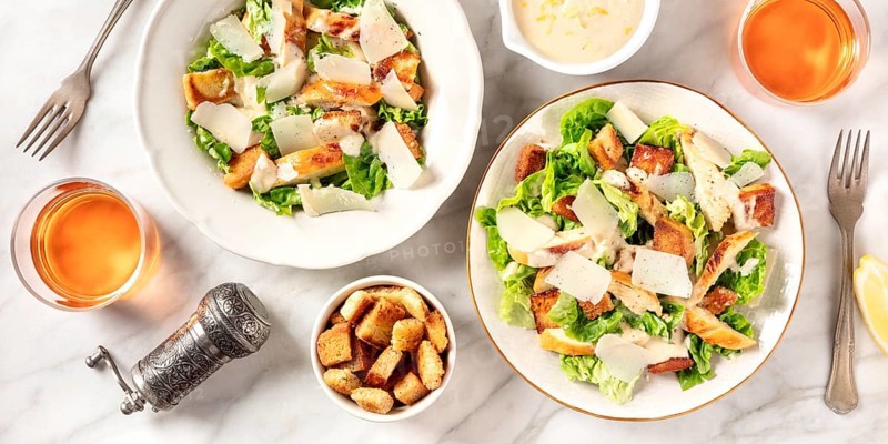 Caesar salad panorama with the classic sauce and wine, shot from above on a white marble background