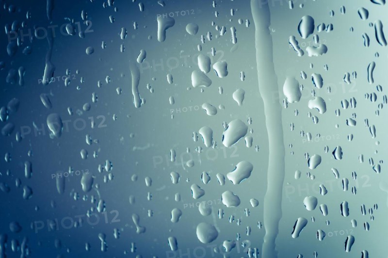 Close up of splashes of water and waterdrops running down on glass panel of bathtub in bathroom while taking a shower