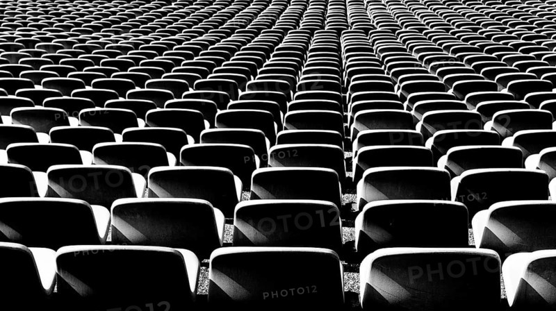 A black and white view of endless rows of empty chairs in a stadium