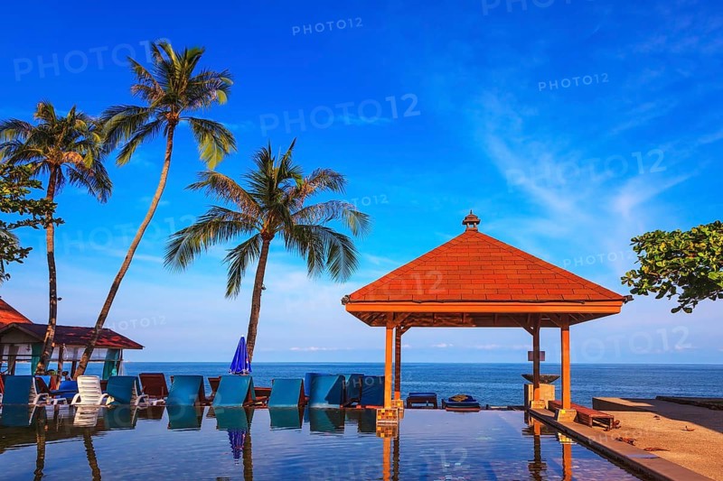 Rest of the Andaman Sea. Popular resort on the island of Koh Samui. Pool surrounded by palm trees on the sea beach. On the edge of the pool red sun canopy