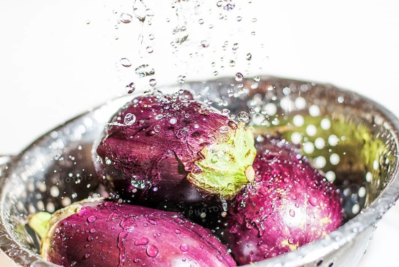 Eggplants being washed in colander under tap fresh water