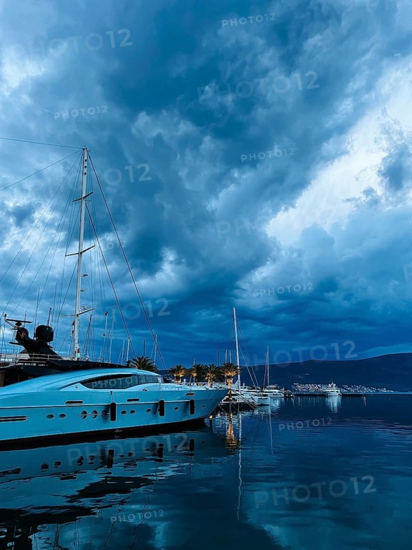 White motor yacht stands on the pier against the background of a twilight dark sky.