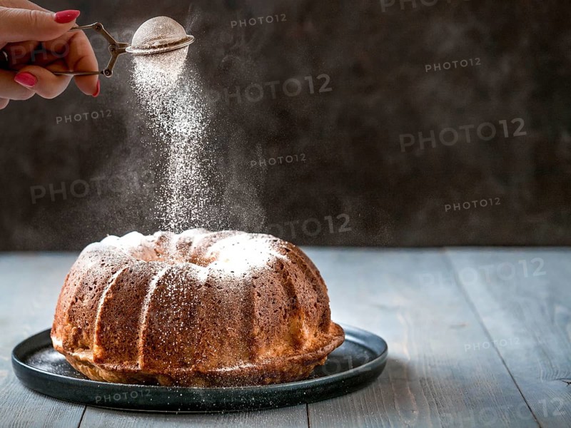 Woman's hand sprinkling icing sugar over fresh muffin cake. Powder sugar falls on fresh perfect muffin cake. Copy space for text. Ideas and recipes for breakfast or dessert