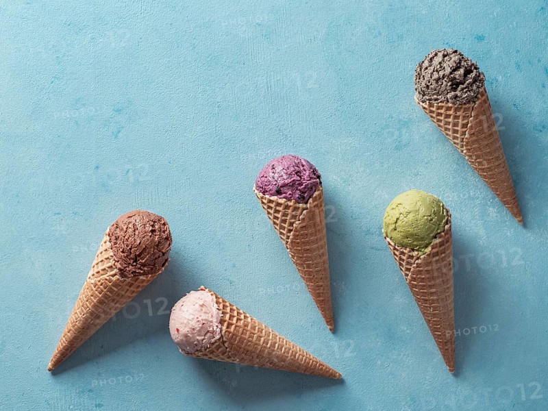 Various ice cream scoops in cones with copy space. Colorful ice cream in cones chocolate, strawberry, blueberry, pistachio or matcha, biscuits chocolate sandwich cookies on blue background. Top view