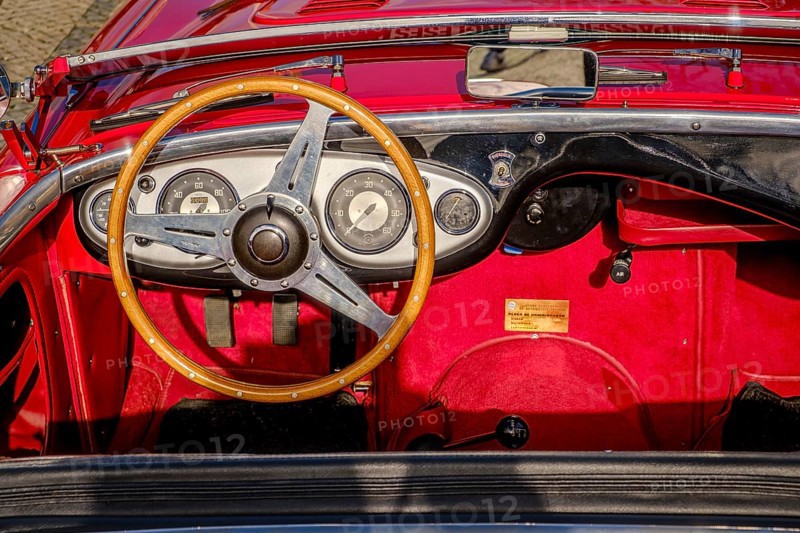 Lisbon, Portugal, Jan 20, 2024: All-red interior of Austin-Healey 100 vintage convertible sports car parked on cobblestone pavement road. Red velvet and leather, wooden steering wheel, fold-down windshield, Europe