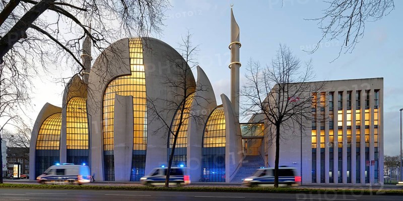 Several police vehicles with flashing lights drive past the Kölne Mosque in Ehrenfeld