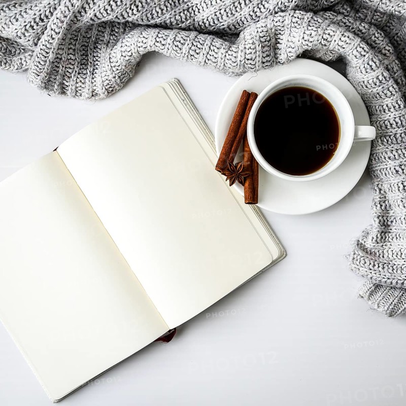 Cup of coffee with notebook cinnamon sticks and anise star on white background. Sweater around. Winter morning routine. Coffee break. Copy space. Top view. Breakfast. Flat lay