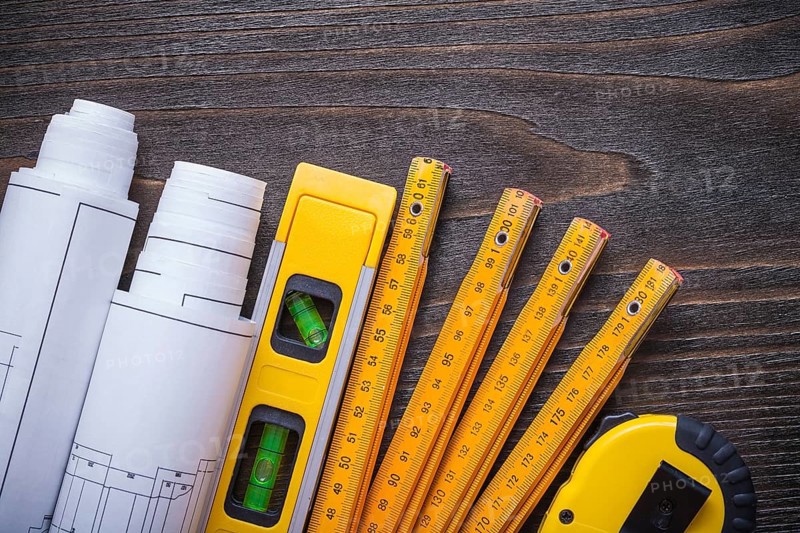 Close up view of blueprint rolls construction level tape-line and wooden meter on vintage wood board maintenance concept