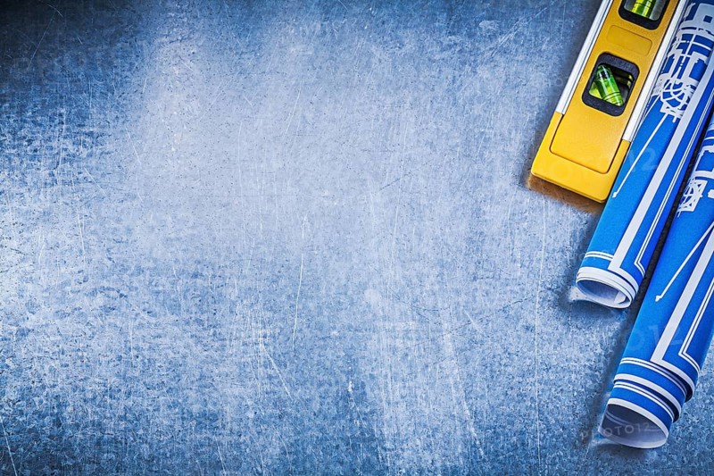 Rolled up blue blueprints construction level on metallic background copyspace