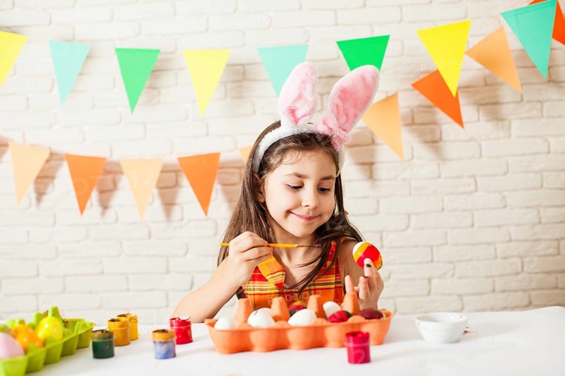 Girl with Easter bunny ears is painting colorful Easter eggs at home. Easter decorations and preparations