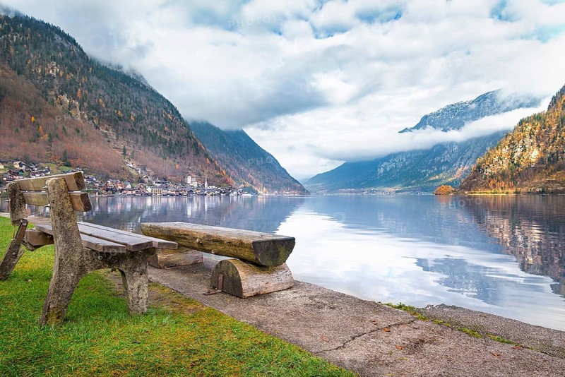 Travel destinations theme image with the Dachstein Mountains reflected in the water of the Hallstatter lake and wooden benches on its shore, in Hallstatt, Austria, Europe