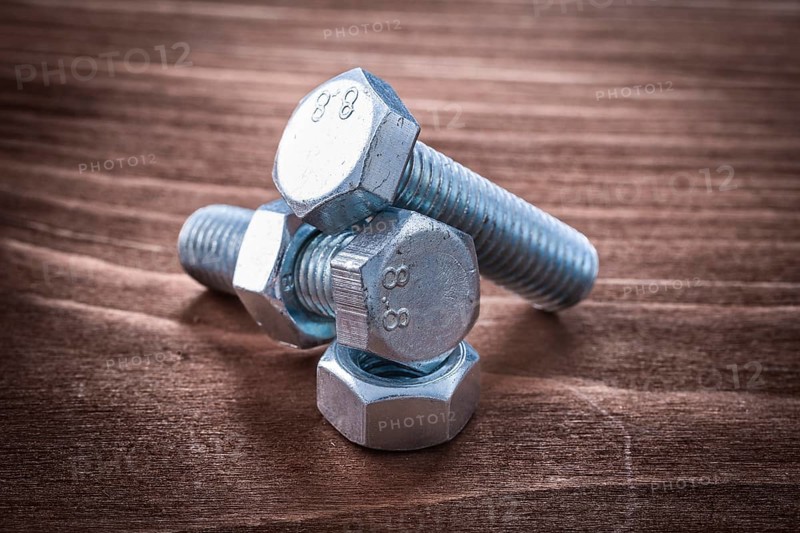 Couple of threaded metal bolts and screw nuts on vintage wooden board repairing concept
