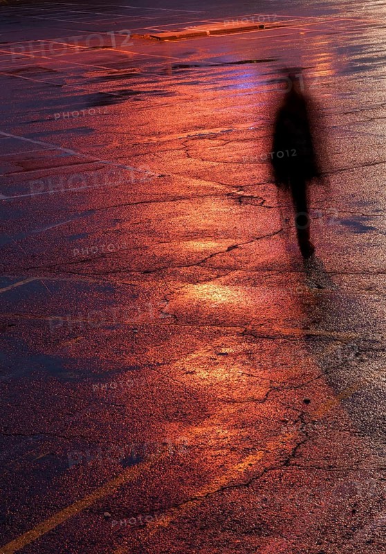 Unrecognised person walking alone in the dark under bright orange light after rain