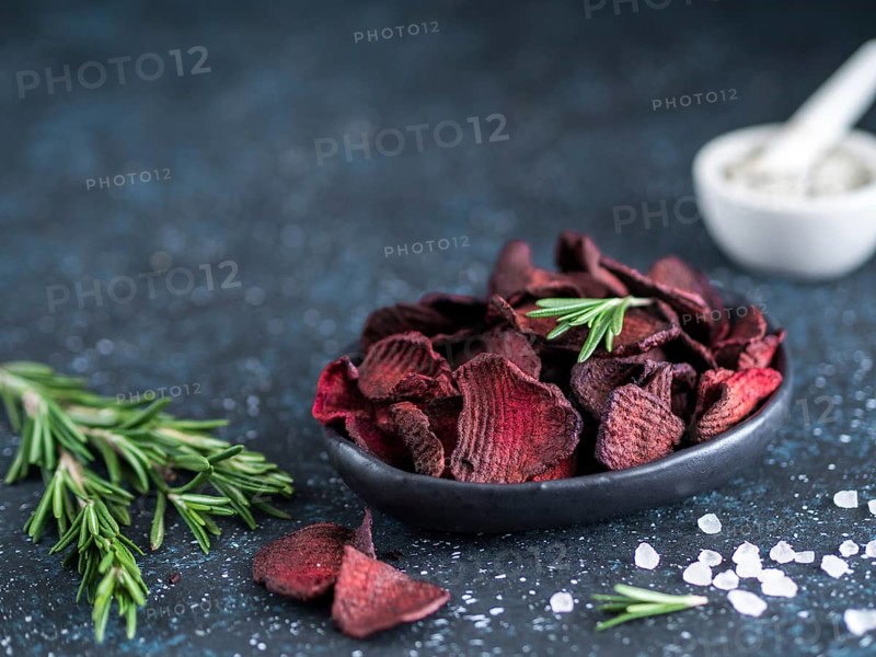 Baked beet slices with coarse sea salt scented rosemary. Vegan diet food idea and recipe. Healthy homemade beetroot chips in plate and ingredients on dark blue background. Copy space
