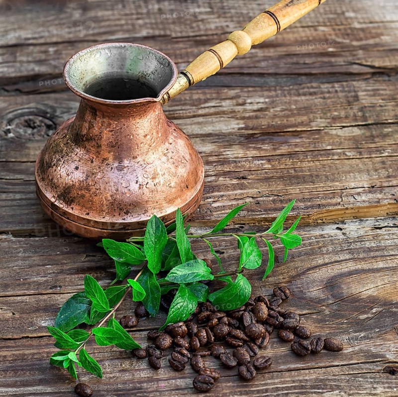 Vintage copper Turk on wooden background covered coffee beans with mint petals