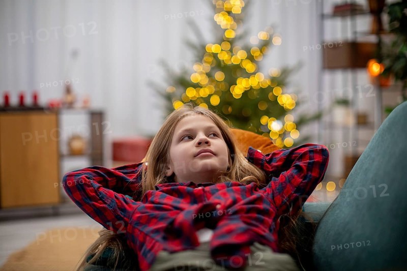 A joyful child relaxes in a cozy, warm setting, surrounded by festive decorations and glowing lights