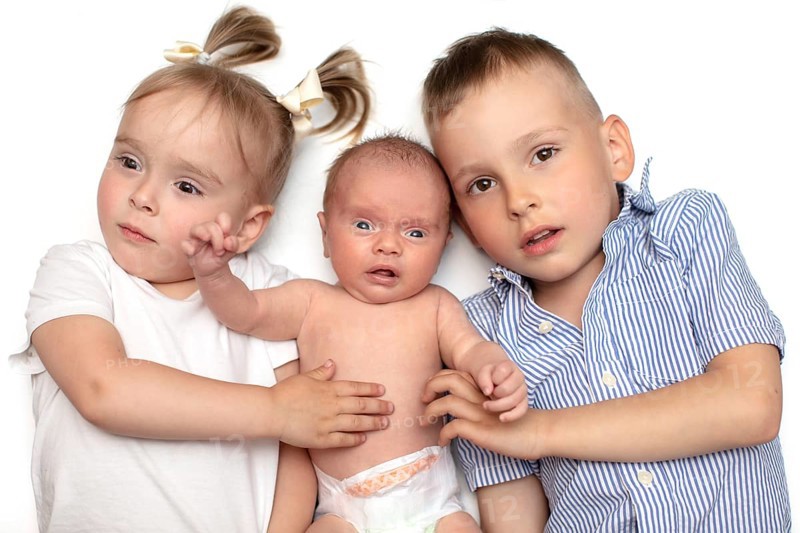 Brother and sister lying together with a newborn baby. Three small children of different ages. Children in the family