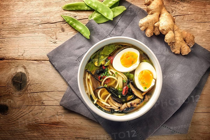 Miso soup with noodles, nori seaweed, snow peas, ginger and an egg in a bowl on a rustic wooden table, top view from above, copy space, selected focus