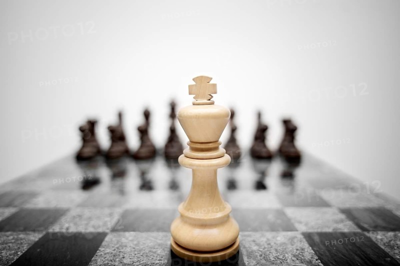 The expressive photo of the chess king standing in front of the set of pieces of a different colour