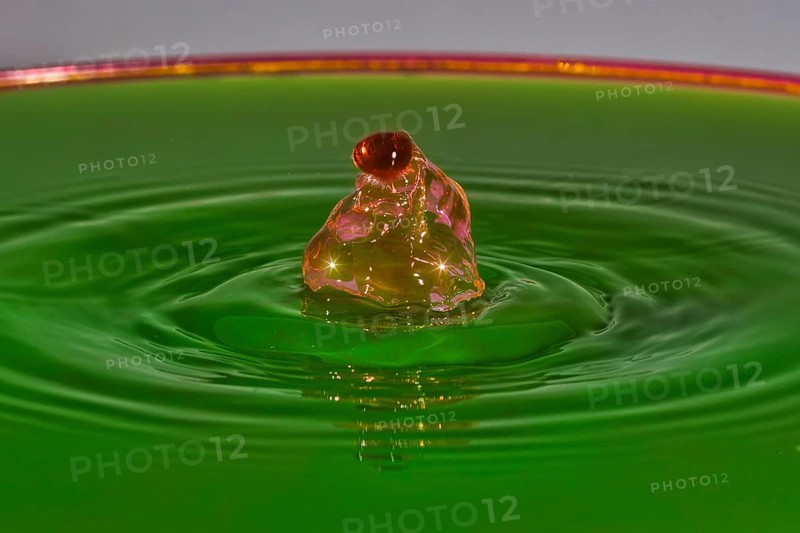 A reddish-brown drop hits green liquid and forms water rings, water droplets, collision, high-speed photography, concept