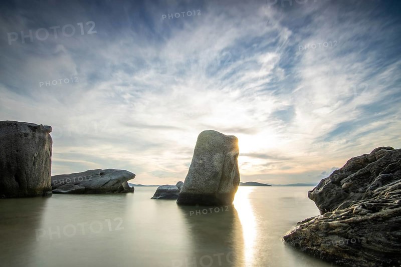 View through rocks on a sandy beach into the sunset. Landscape shot with view to the horizon over the wide sea at the coast of Ouranoupoli, Thessaloniki, Central Macedonia, Greece, Europe