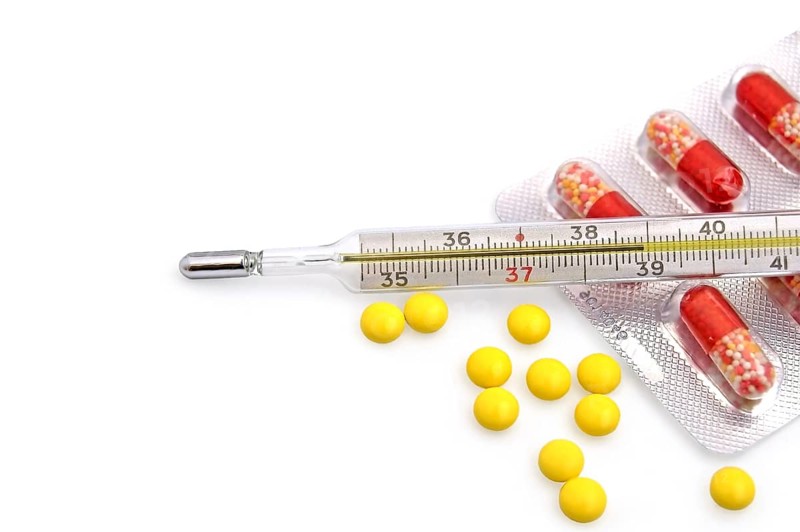 Thermometer with the yellow pills in bulk and red-white capsules in a package on a white background, Russia, Europe