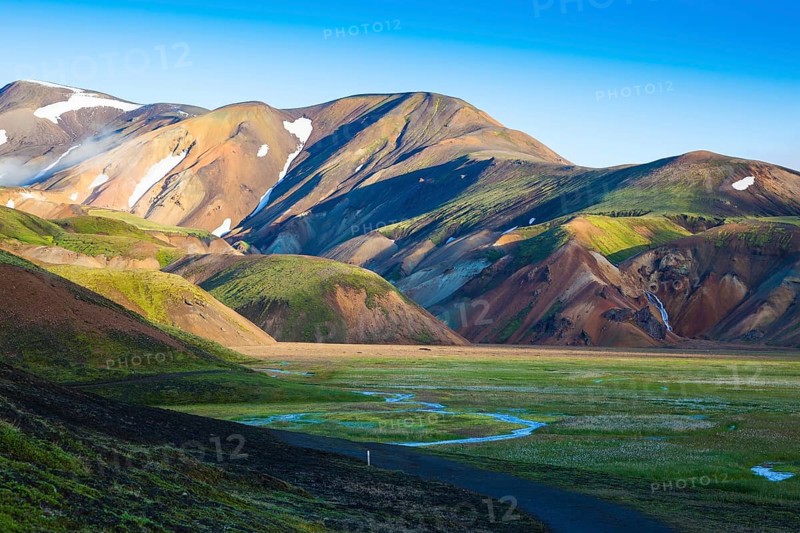 Snow lies in the hollows of colorful rhyolite mountains. Green Valley is flooded with melt water. Early summer morning in the National Park Landmannalaugar, Iceland, Europe