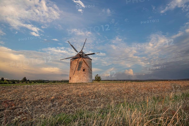Windmill with wooden sails in a landscape with fields. Meadows and flowers appear in the sunset. Landscape shot in nature with a windmill. Historically atypical for the Balaton region in Hungary