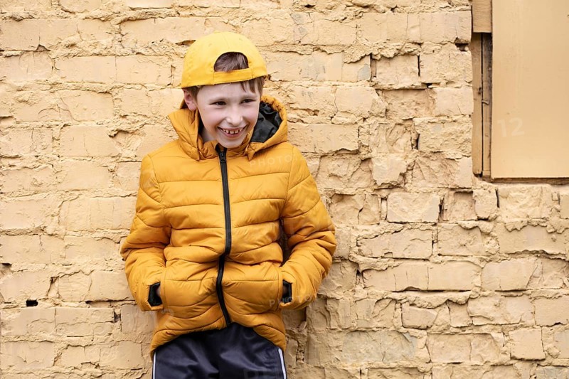 A child on the street A cheerful boy in yellow clothes and a baseball cap stands against a brick wall