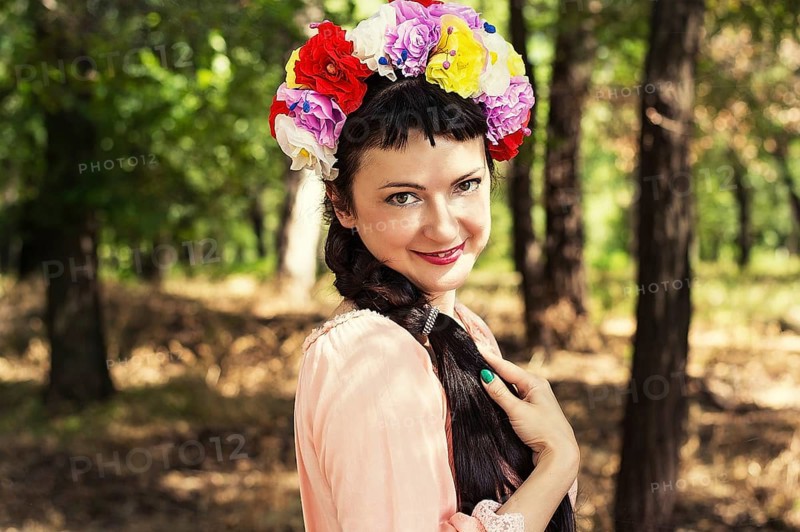 Charming woman in wreath of roses on her head on the background of nature