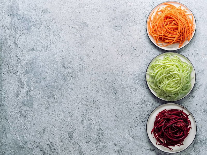 Vegetable noodles - zucchini, carrot, and beetroot noodles on plate over gray cement background. Clean eating, raw vegetarian, food concept. Copy space for text. Top view or flat lay