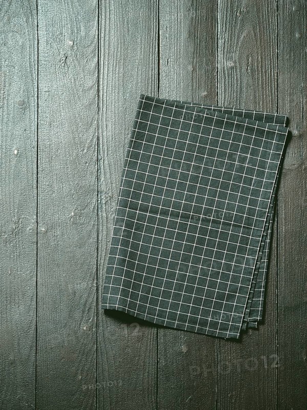 Dark wooden table with balck and white dark linen kitchen towel or textile napkin flat lay. Dark tablecloth on brown gray wood tabletop. Copy space for text. Can use as mock up for design. Vertical