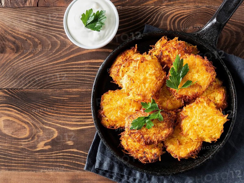 Potatoes pancakes latkes, flapjacks, hash brown or potato vada with white greek yoghurt or sour cream on brown wooden table. Copy space for text