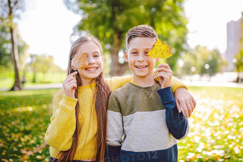 Friendship between siblings. Siblings together outside with bright coloured background. Kids autumn portrait. Brother and sister playing in autumn park leaves. Family active fall weekend concept