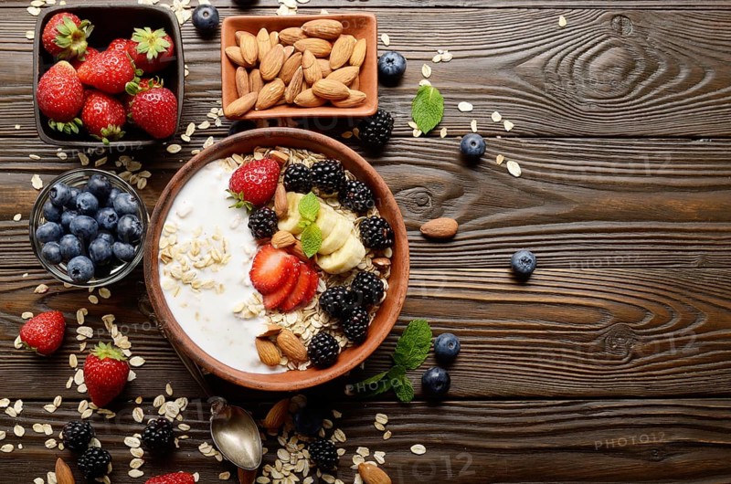 Flat lay top view at Fruit healthy muesli with banana strawberry almonds and blackberry with yogurt in clay dish on wooden kitchen table