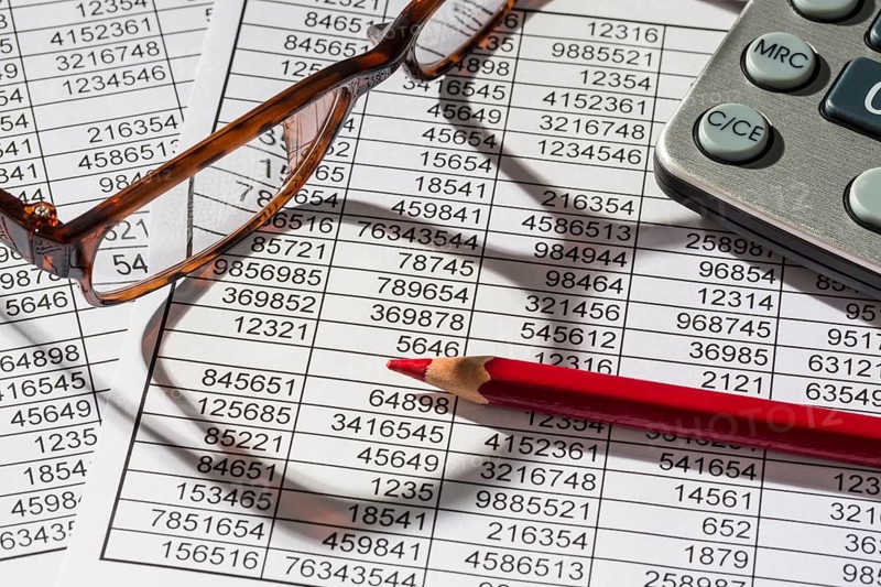 A calculator lies on the figures of a balance sheet and statistics. Symbol photo for turnover, profit and costs
