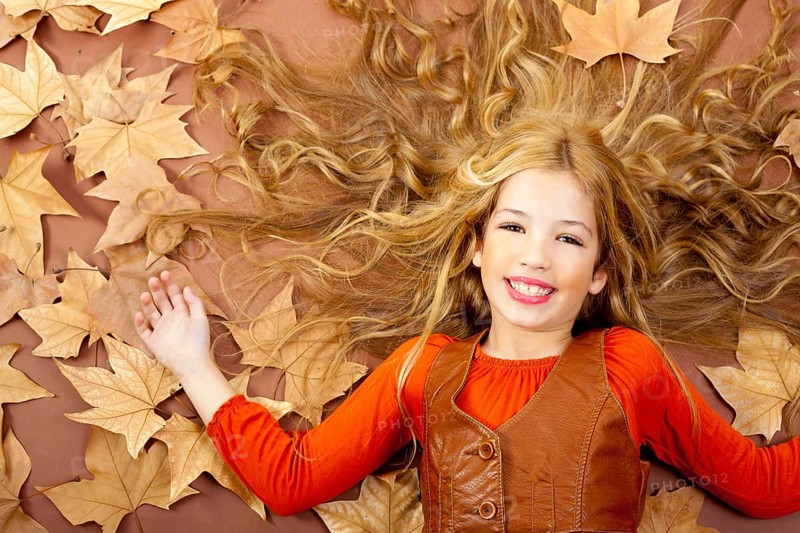Autumn fall little blond girl on dried tree leaves background and long spread hair