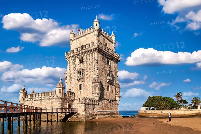 Belem tower and wooden bridge to it, Lisbon, Portugal at blue summer day sky with clouds. Medieval fort on Tagus river in late Gothic or Manueline style, UNESCO world heritage site, Age of Discoveries, tourist attraction, Portuguese seafaring history